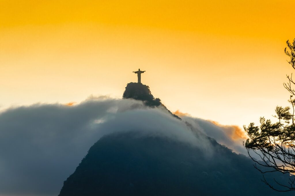 Cristo Redentor visto junto com o por do sol. Núvens ao redor da Floresta da Tijuca.