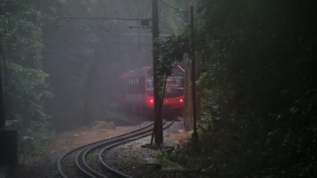 Trem do Corcovado saindo de trás das árvores, a floresta da Tijuca está umida e escura. farois do trem acesos.