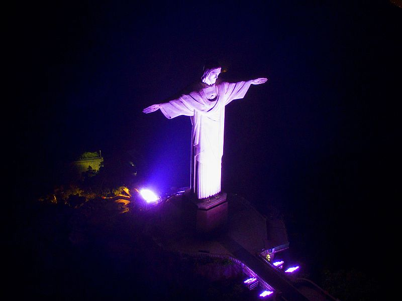 Foto noturna do Cristo Redentor Iluminado em tom lilás. 