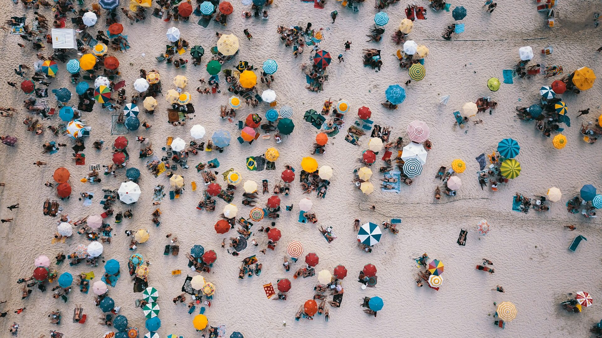 Foto da areia da praia lota de de guarda sois coloridos.