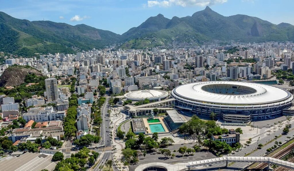 Estádio do Maracanã, foto em dia de sol. Ao fundo a cidade do Rio de Janeiro e as montanhas.