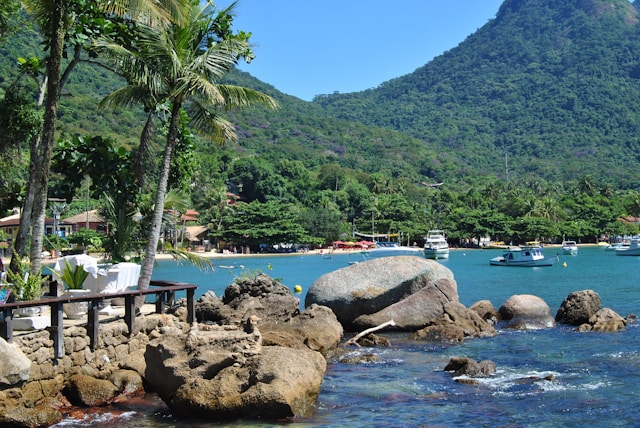 Mostra foto em angulo aberto de ilha de Angra. barcos no mar, dia de sol.