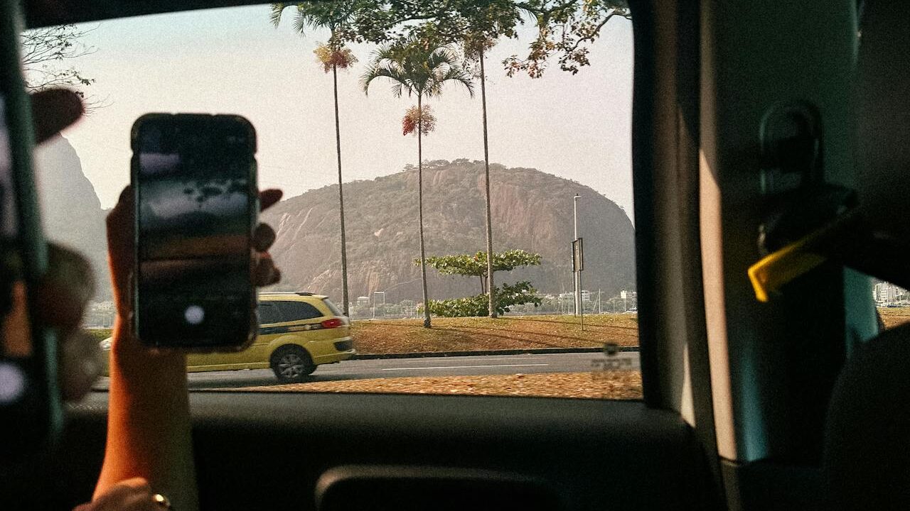 Foto de pessoa dentro de um carro vendo um táxi no Rio de janeiro pela janela do carro.