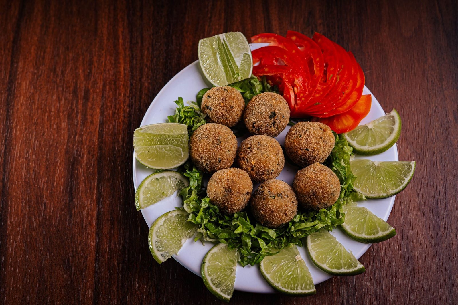 Comidas Típicas do Rio de Janeiro: o Que Comer na Cidade 2 Bolinhos de bacalhau dourados servidos com limão e tomate, petisco típico de boteco carioca